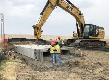 excavator lifting beams with construction workers at IH 35E